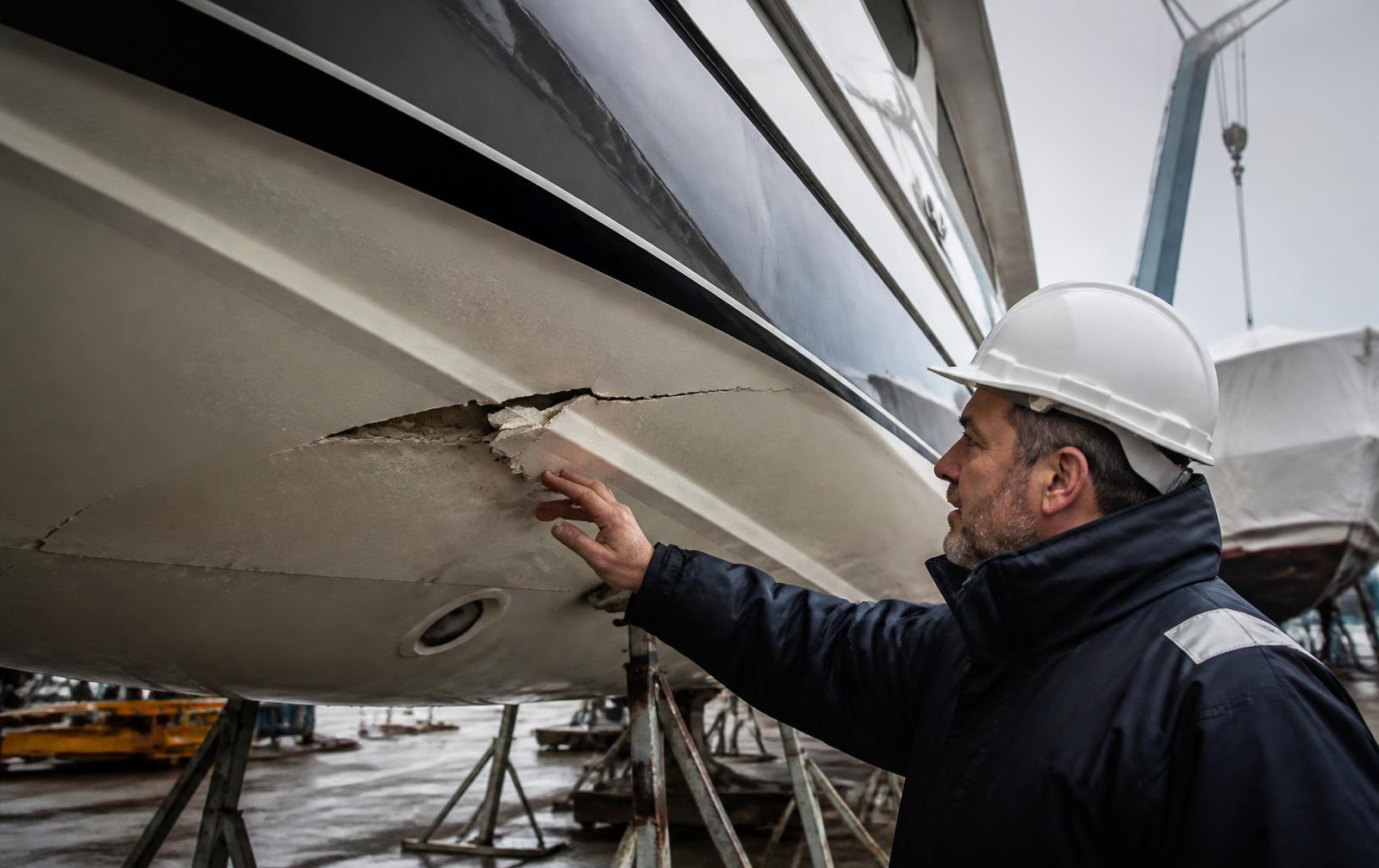 Surveyor examining impact damage on a yacht hull in a shipyard